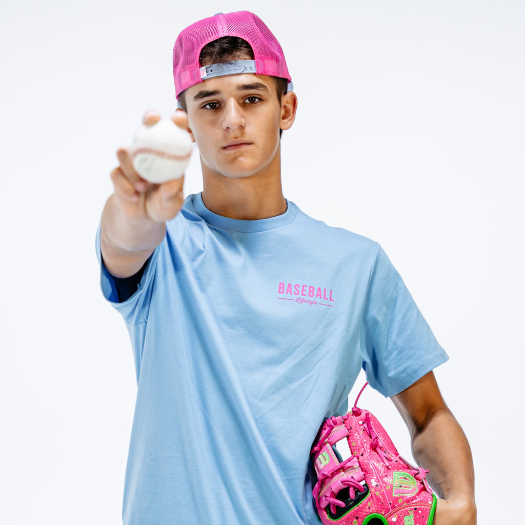 Person wearing a light blue 'BASEBALL' t-shirt and pink cap, holding a baseball and pink glove.