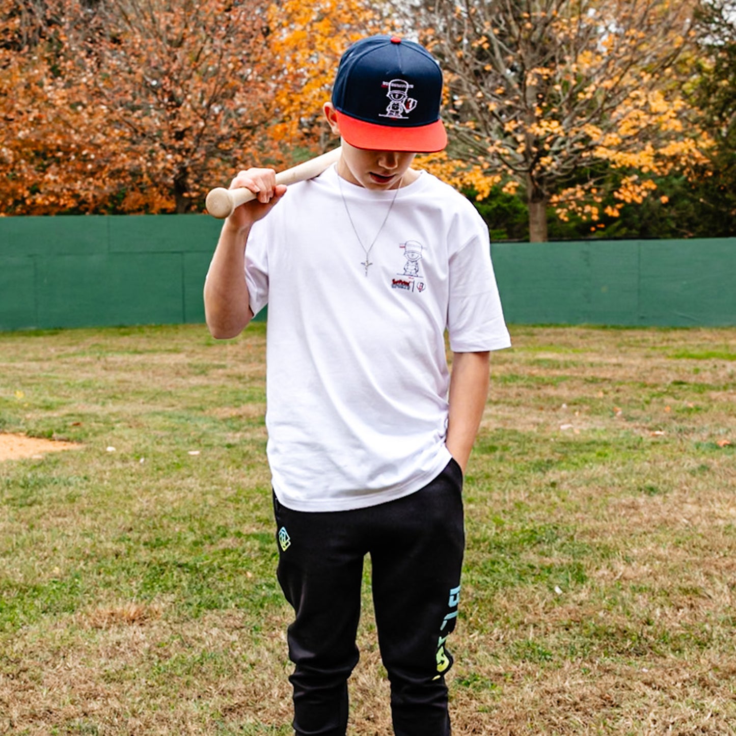 Person holding a baseball bat wearing whit Pablo Sanchez t-shirt in a grassy field with trees in the background