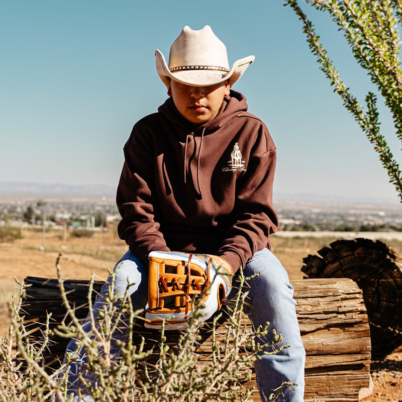 Person wearing a brown hoodie with a 'Chasing Spring' horse logo, sitting outdoors with desert landscape in the background