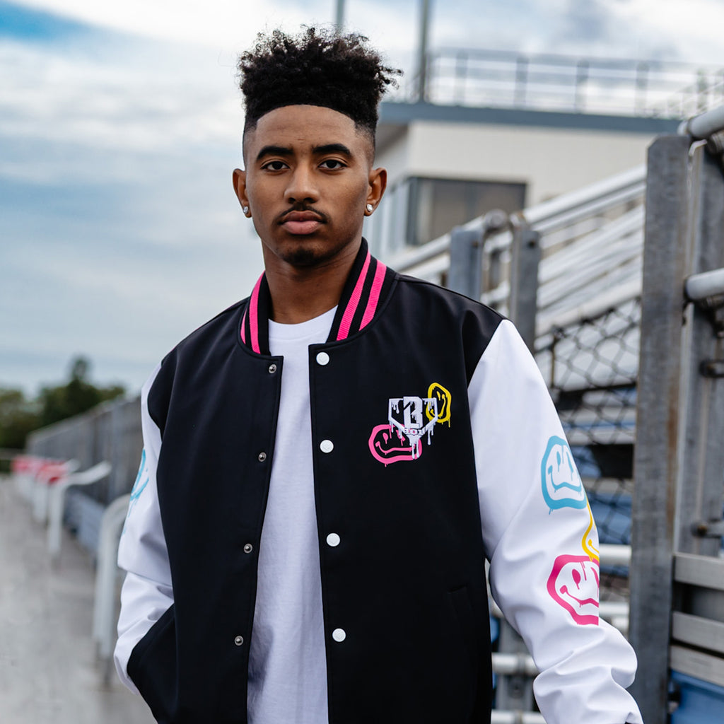 Person wearing a black, pink and white varsity jacket with colorful designs outdoors.