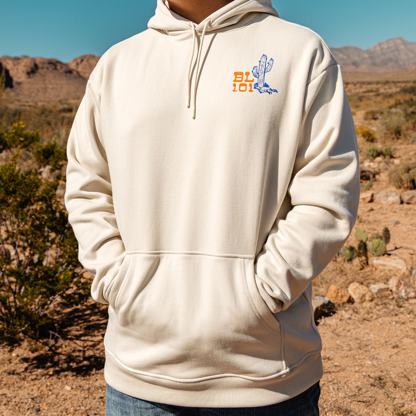 Person wearing a beige hoodie with a logo in a desert setting