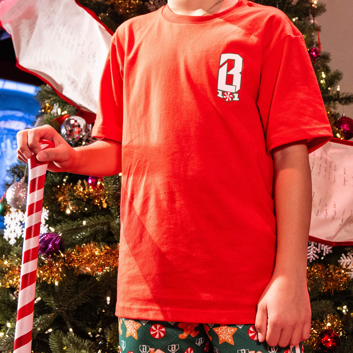 Person wearing a red shirt with a BL101 logo, holding a candy cane, in front of a decorated Christmas tree.
