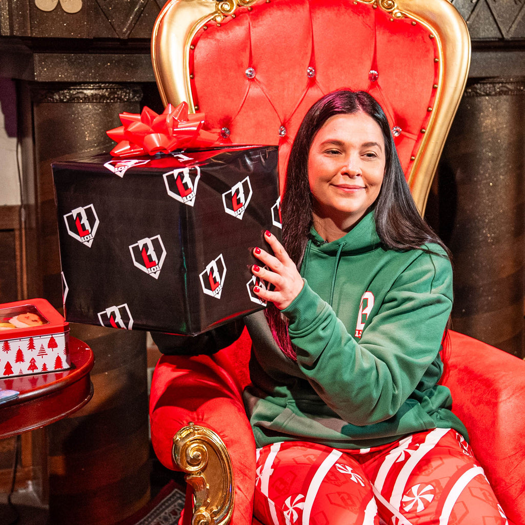 Person holding a large gift box with a red bow on a red throne-like chair.