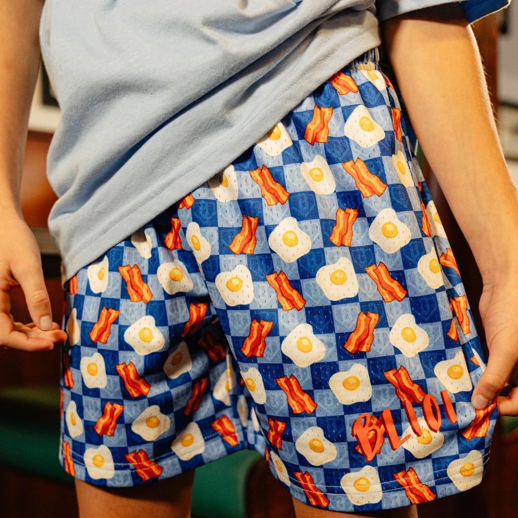 Person wearing blue checkered shorts with a bacon and egg pattern 