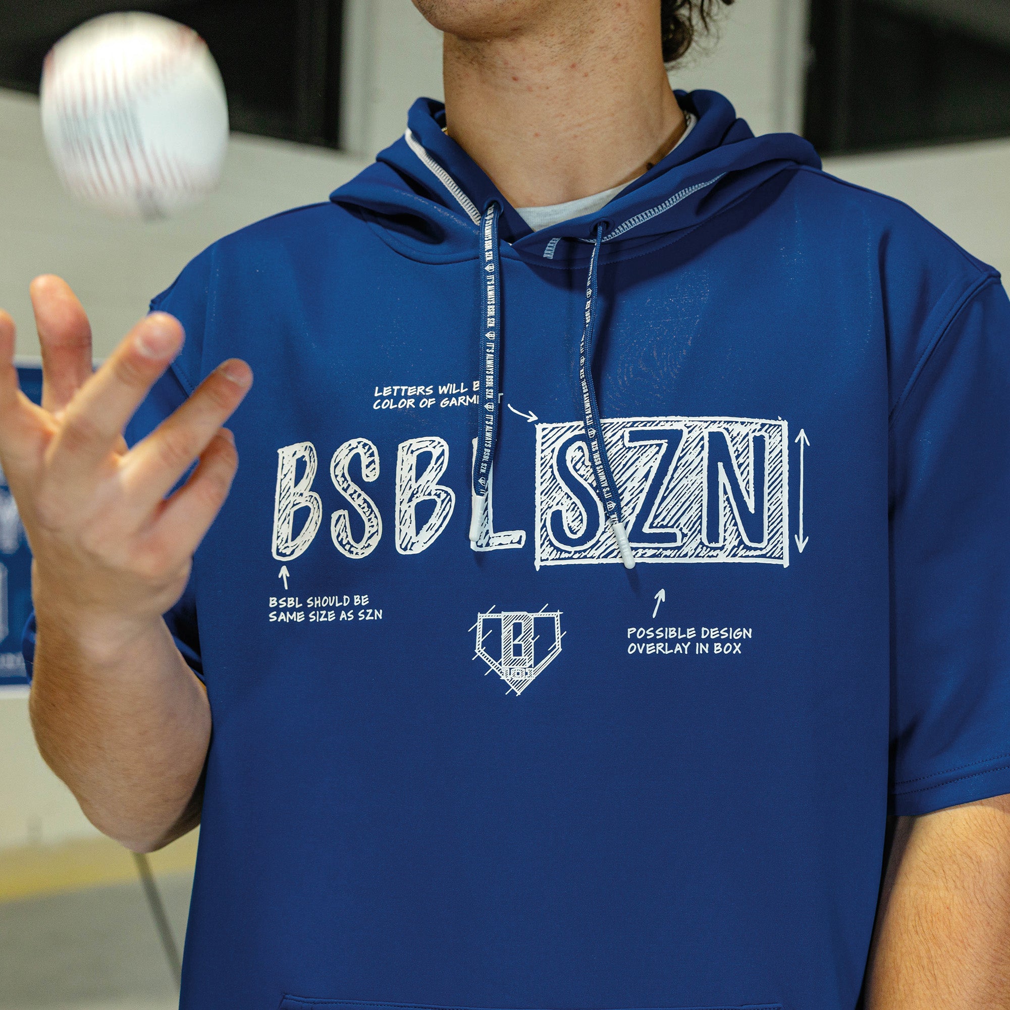 Person wearing a navy shorts sleeve blue hoodie with white blueprint 'BSBL SZN' text and white 'bsbl v3' logo