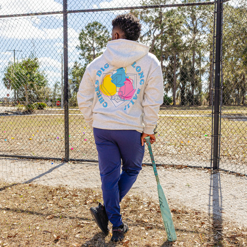 Person wearing a hoodie with a colorful peeps graphic design and 'Chicks dig the long ball!" text on the back in an outdoor setting.