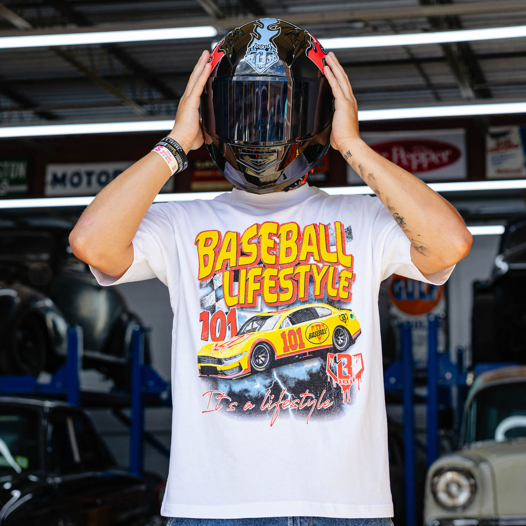 White Diamond Drift tee showing full yellow and red BL101 race car graphic, model putting on racing helmet in vintage garage.