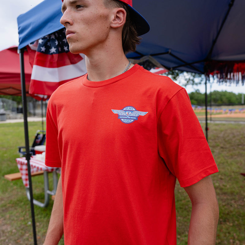 Close-up of adult male model in red Fastball Flight tee showing Air Show Division badge on chest at outdoor event