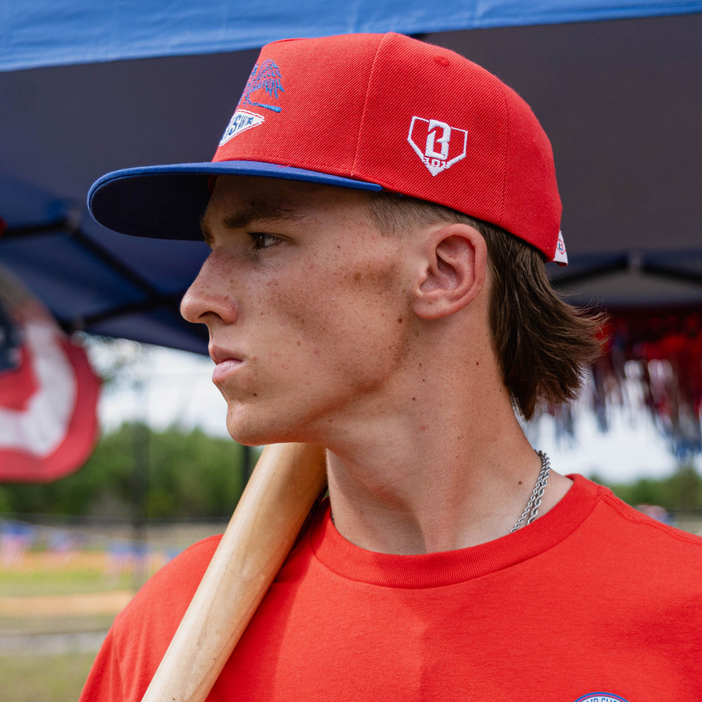 Person wearing a red cap and shirt with a baseball bat, standing outdoors.