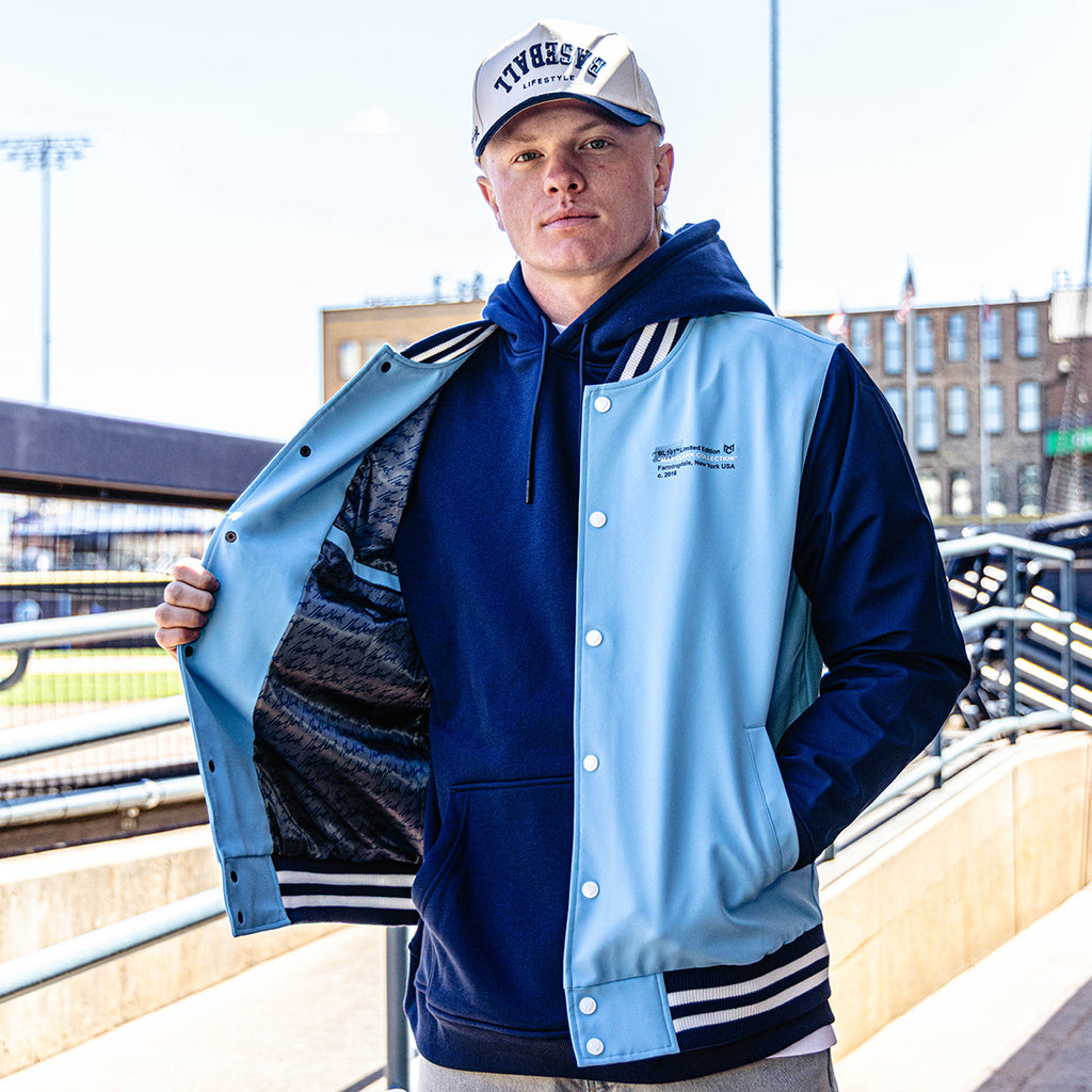 Person wearing a blue and light blue varsity jacket with a cityscape background