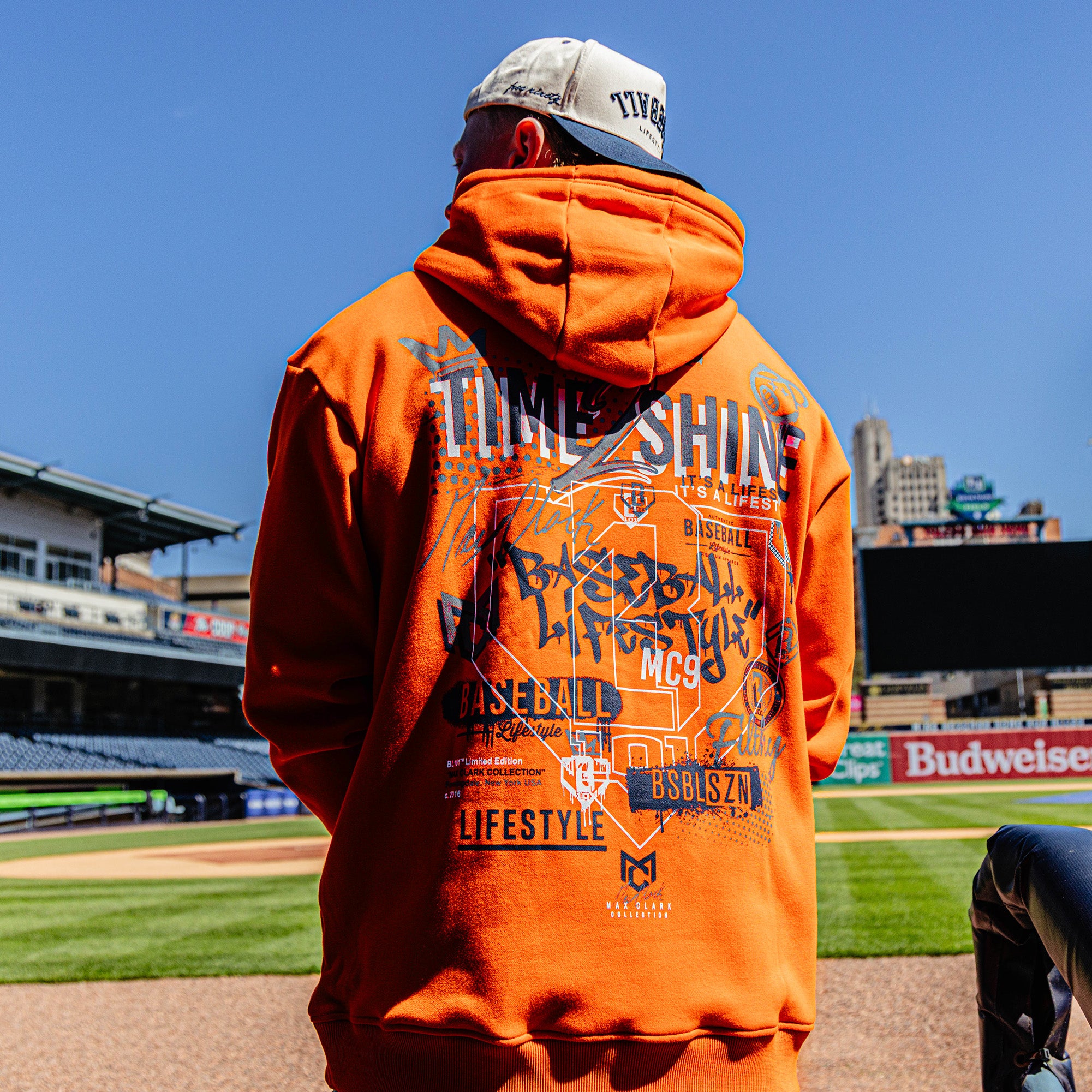Person wearing an orange hoodie with graphics at a baseball stadium