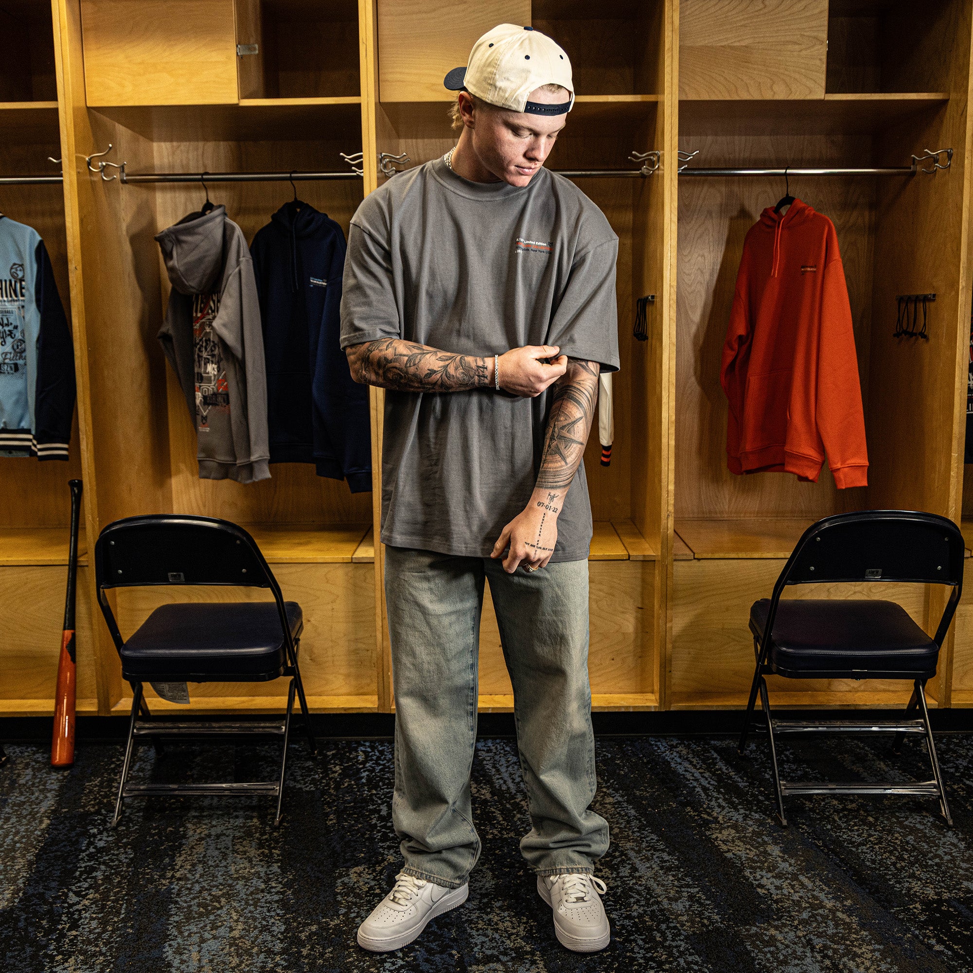 Person standing in a locker room wearing a gray t-shirt and pants.
