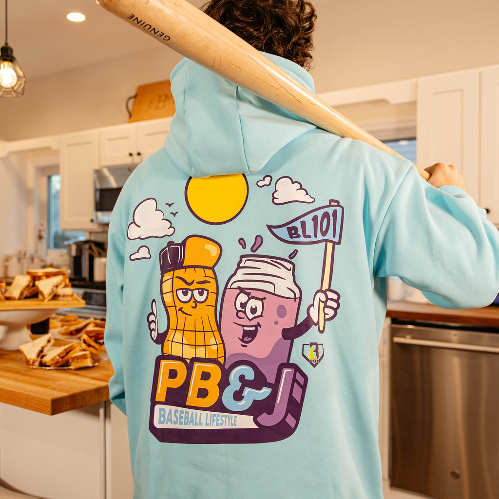 Back view of the BL101 PB&J Baseball Lifestyle light blue hoodie on a male model holding a baseball bat, showing the cartoon peanut and jelly jar mascot graphic.