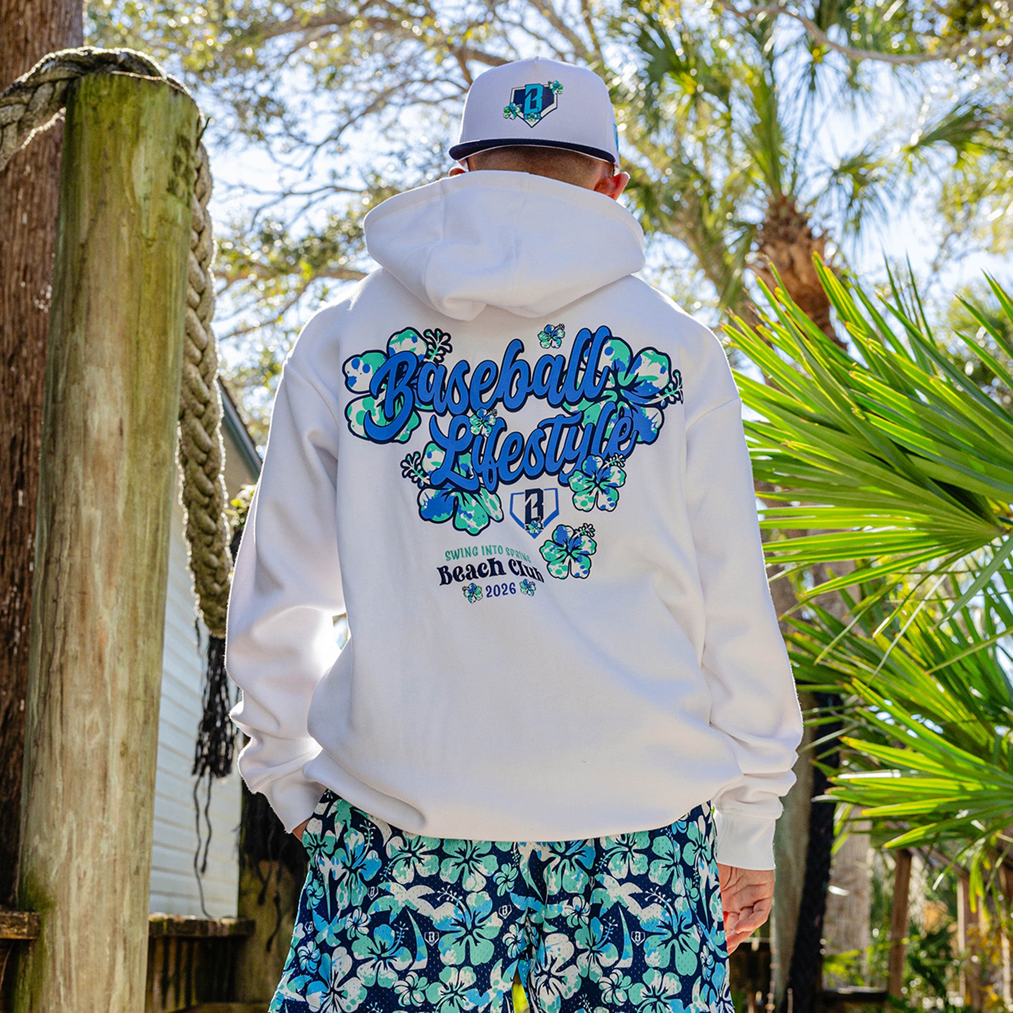 Person wearing a white hoodie with floral 'Baseball Lifestyle Swing Into Spring Beach Club 2026' text