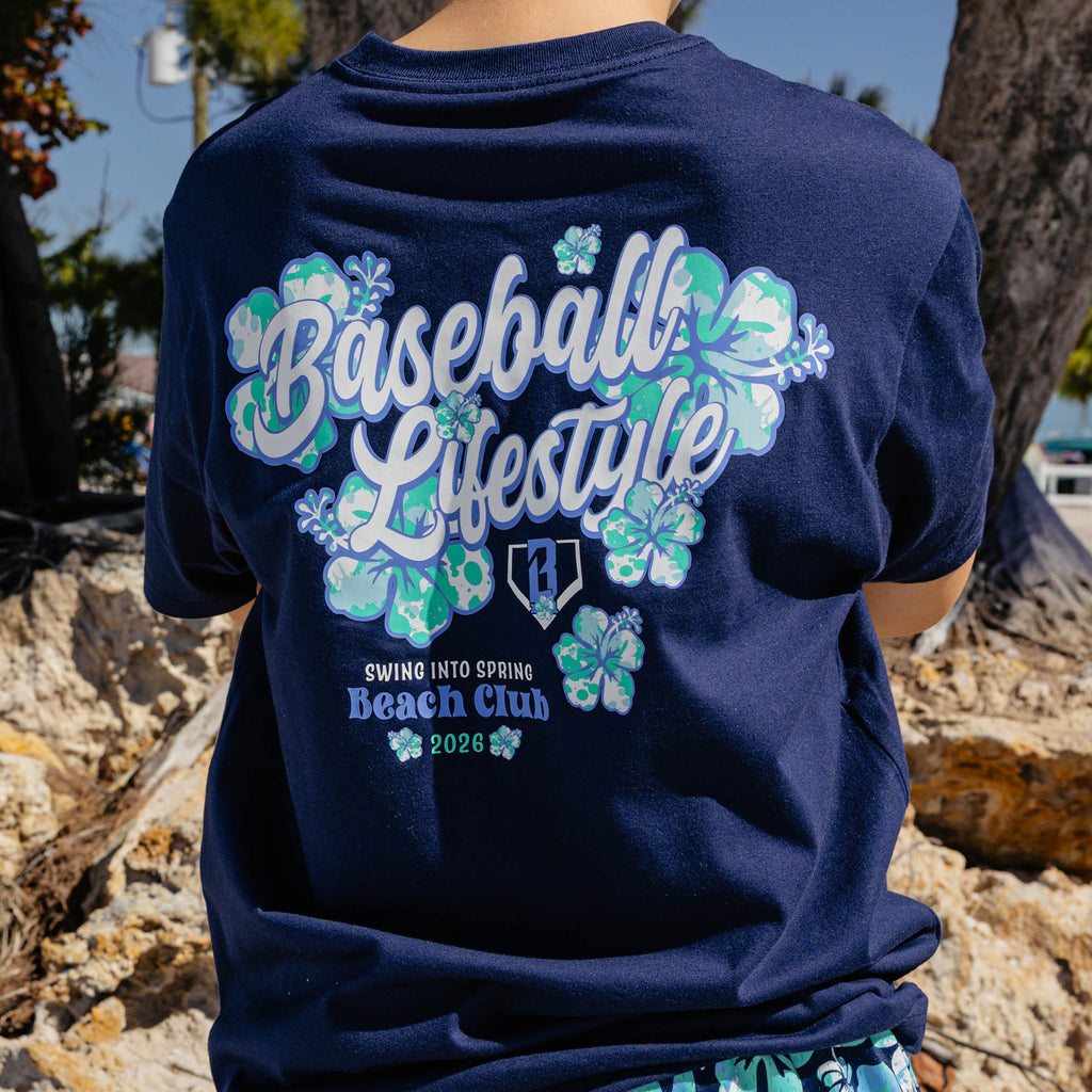 Navy blue t-shirt with floral designs and 'Baseball Lifestyle Swing into Spring Beach Club 2026' text on the back, worn by a person outdoors.