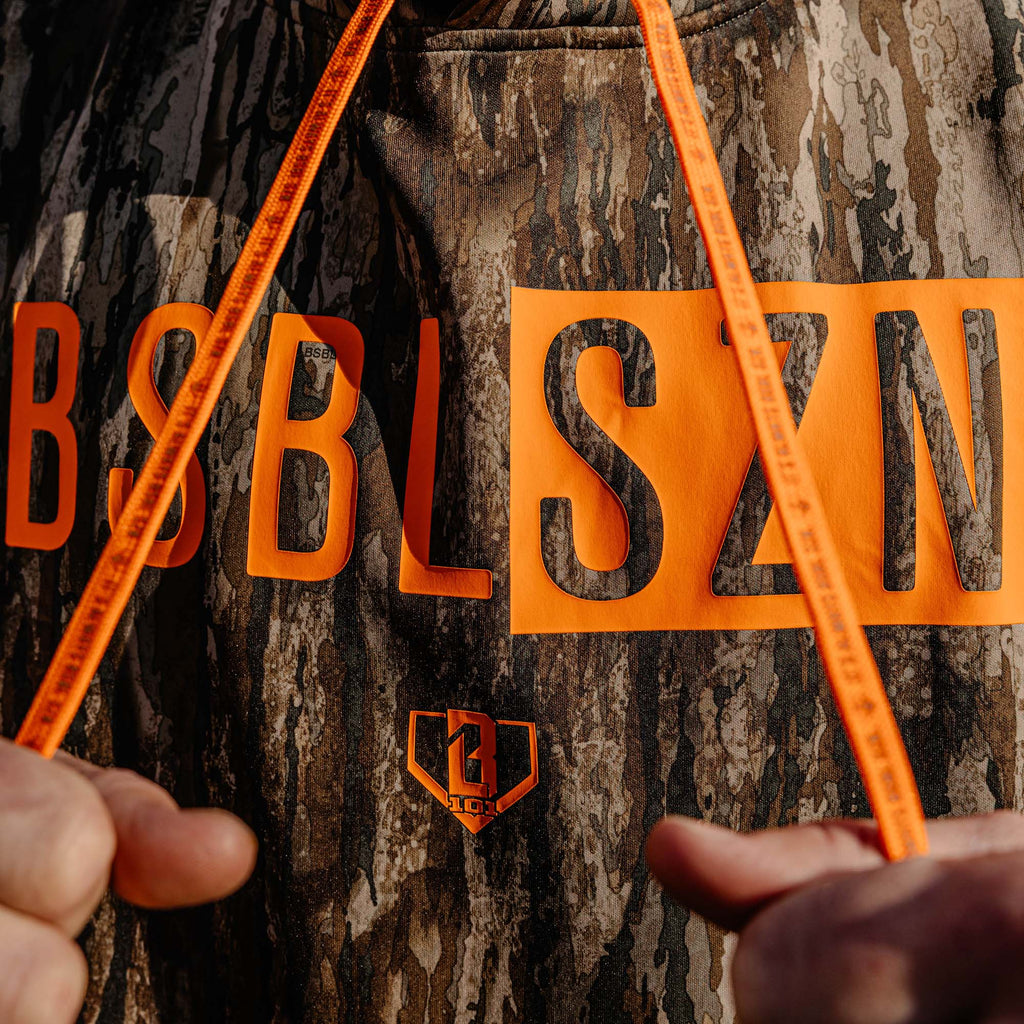 Camouflage jacket with orange 'BSBL SZN' logo held by a person