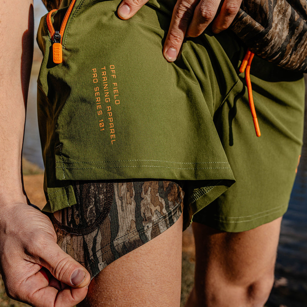 Person wearing green shorts with 'OFF FIELD TRAINING APPAREL PRO SERIES 101' text and orange drawstrings, standing by a body of water.