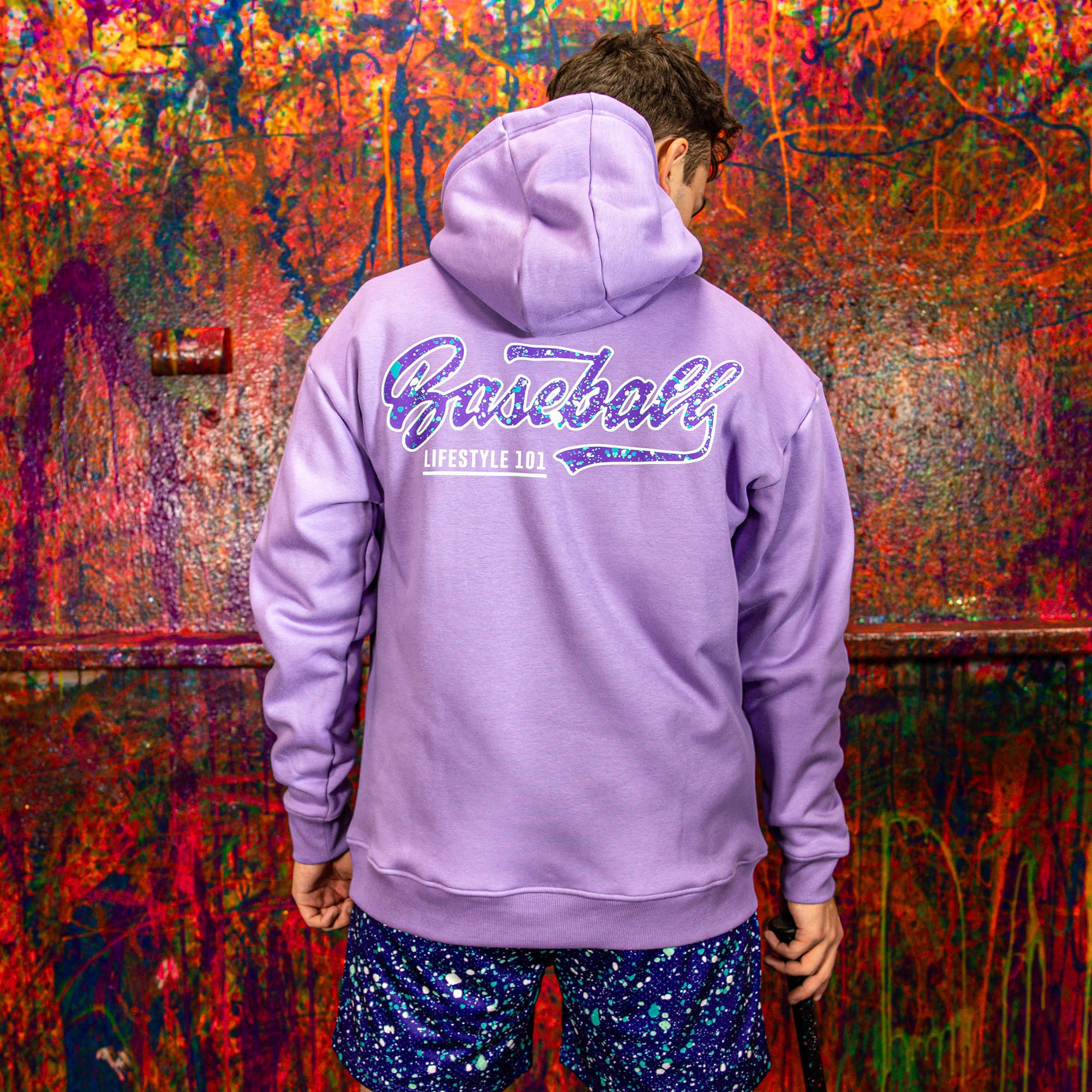 Person wearing a purple hoodie with 'Baseball Lifestyle' text, standing in front of a colorful, abstract wall.