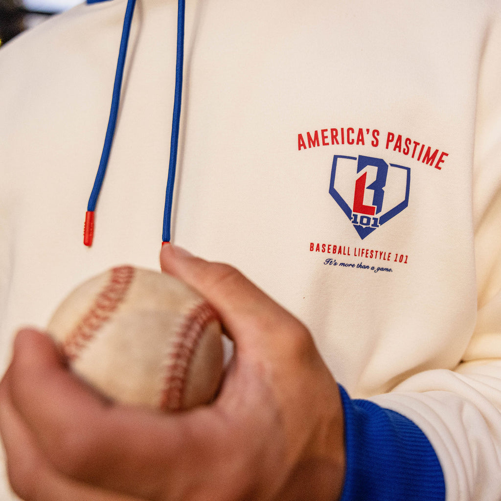 Close up of cream stadium hoodie chest graphic with a hand holding a baseball