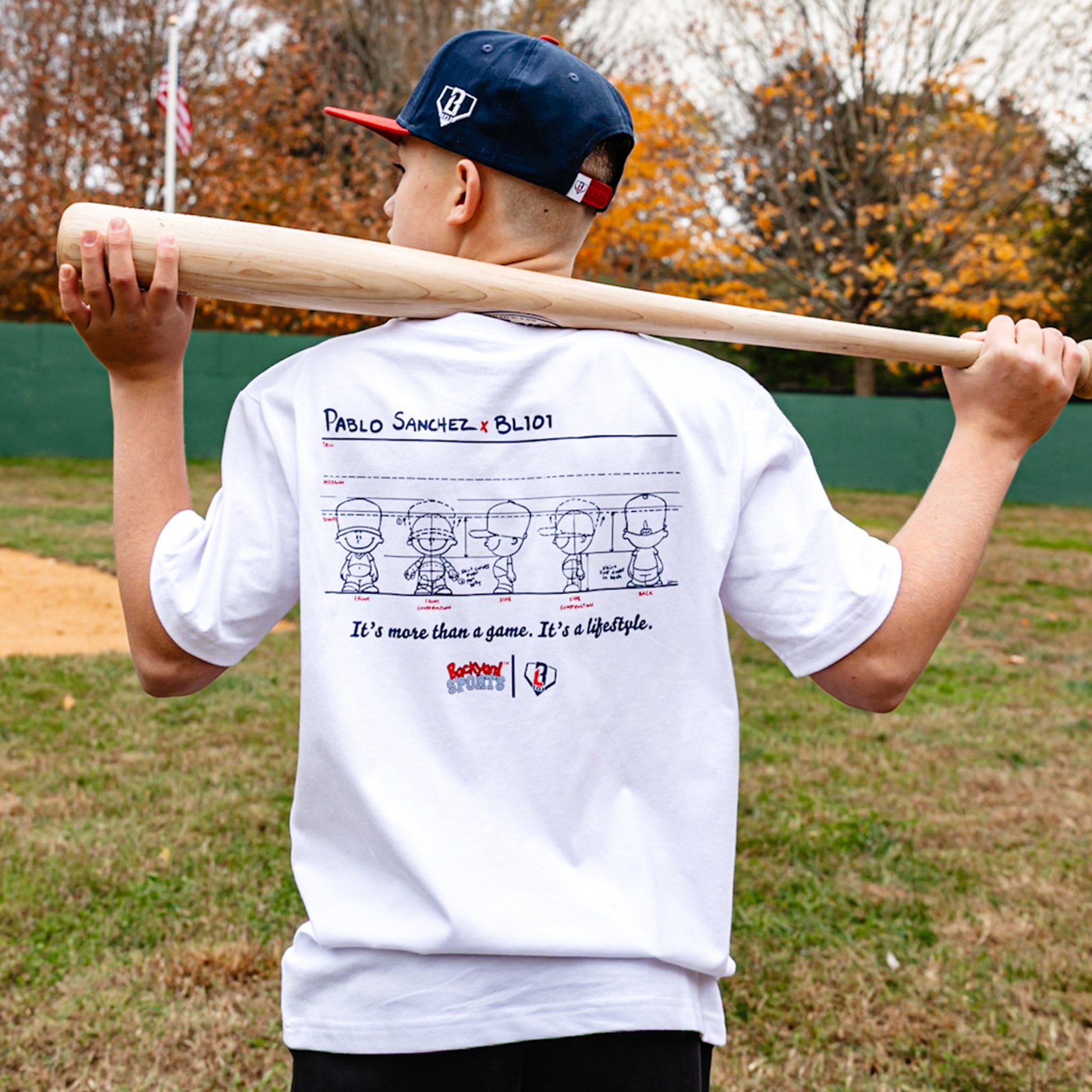 Child holding a baseball bat with a white t-shirt featuring Pablo Sanchez graphics and text on a baseball field.