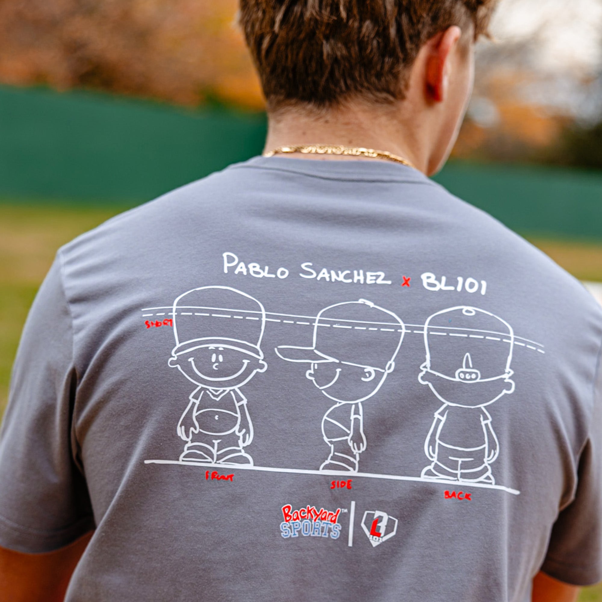 Person wearing a gray t-shirt with Pablo Sanchez graphic and text on the back, standing outdoors.