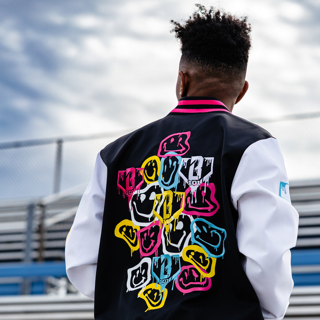 Person wearing a black, pink and white jacket with colorful smiley faces on the back, standing outdoors.