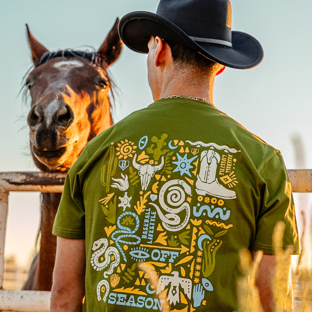 Man wearing a green t-shirt with a desert design, standing next to a horse.