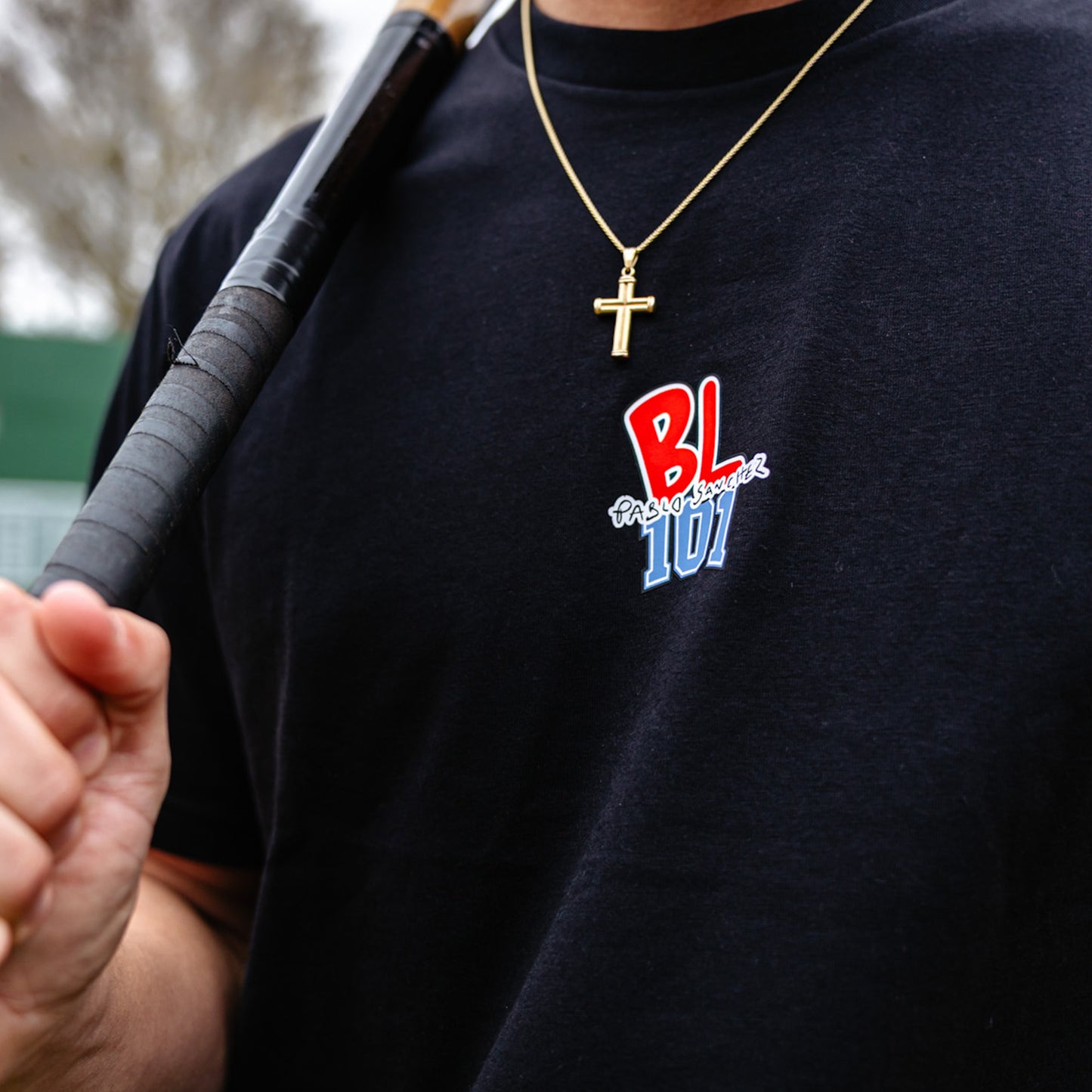 Person wearing a black t-shirt with 'BL101 Pablo Sanchez' logo and holding a baseball bat.