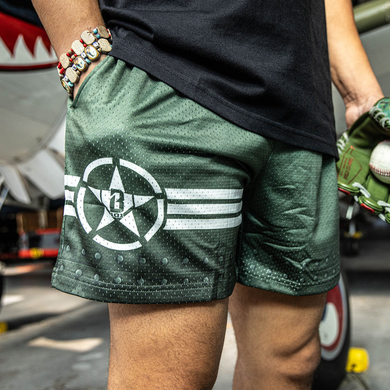 Close up of Green athletic shorts with white waistband, BL101 logo on side, and star logo with stripes on bottom.