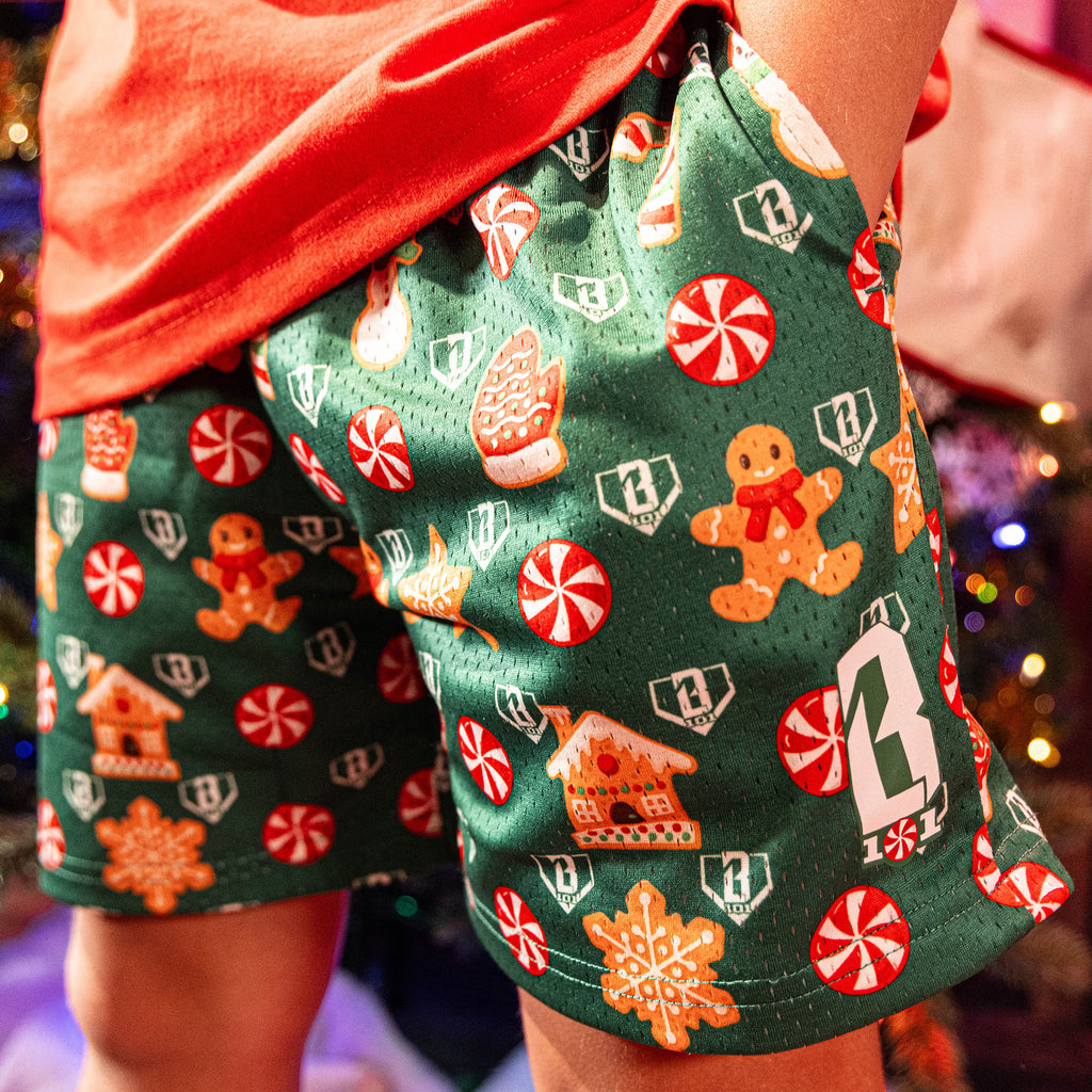 Green shorts with Christmas-themed pattern worn by a person, with blurred festive lights in the background.
