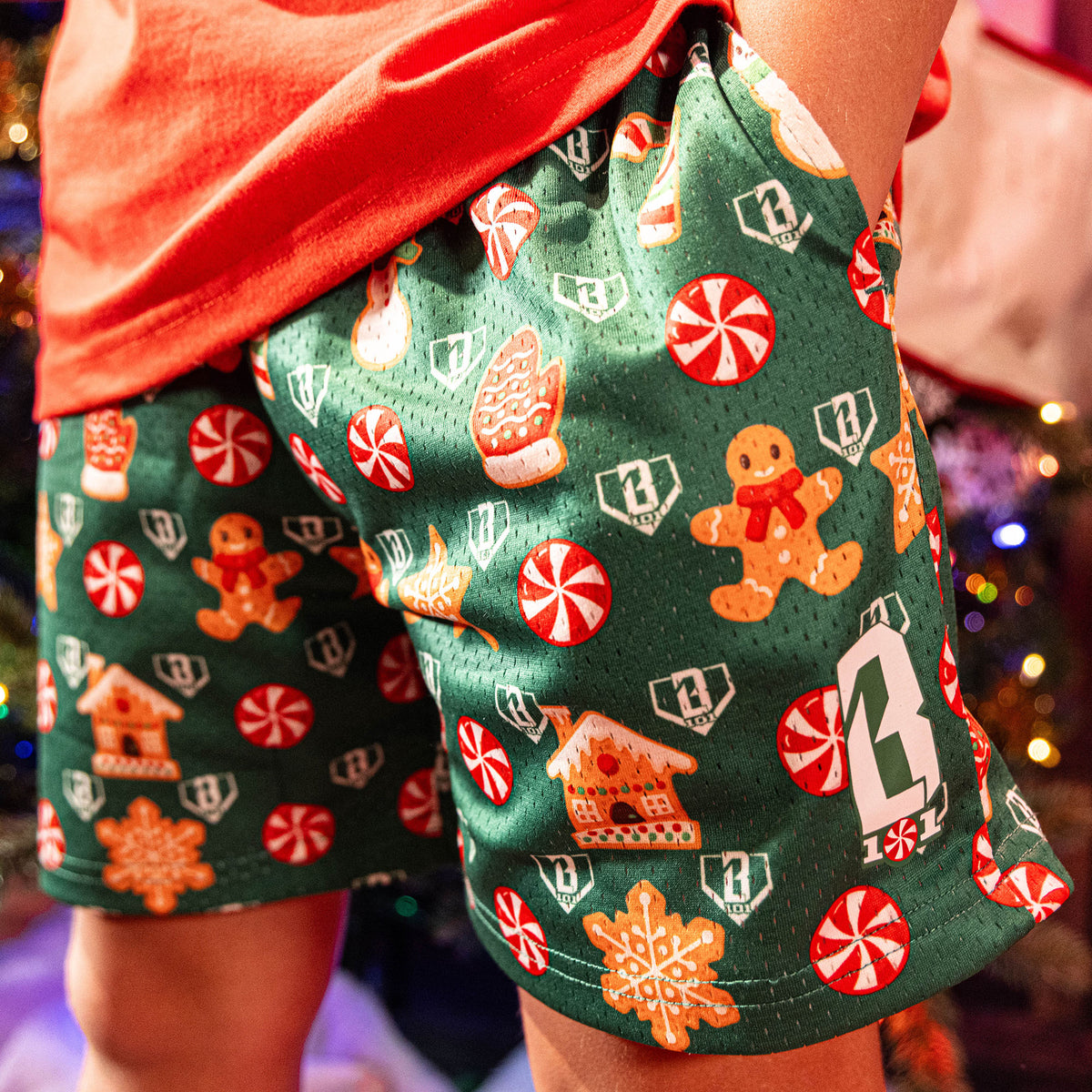 Green shorts with Christmas-themed pattern worn by a person, with blurred festive lights in the background.