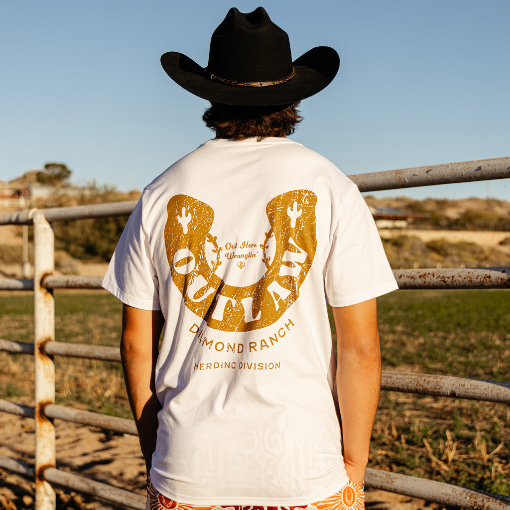 Adult model wearing white graphic tee with “Outlaw Wranglin” design