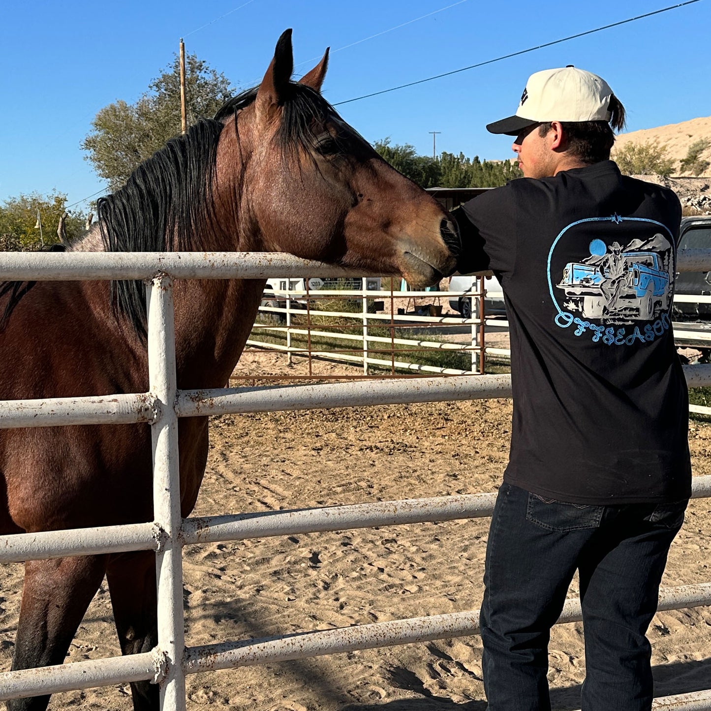 Man standing next to a horse in an outdoor setting in a black t shirt that says 'OFFSEASON'
