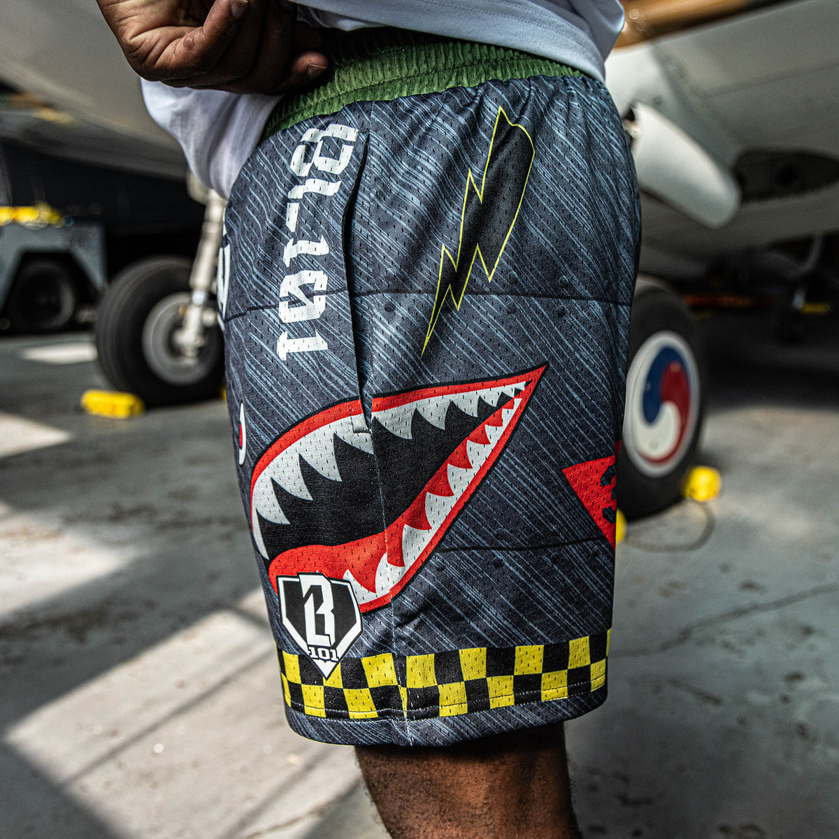 close up of person wearing shorts with a shark mouth graphic and lightning bolt design, with a blurred background of a vehicle.