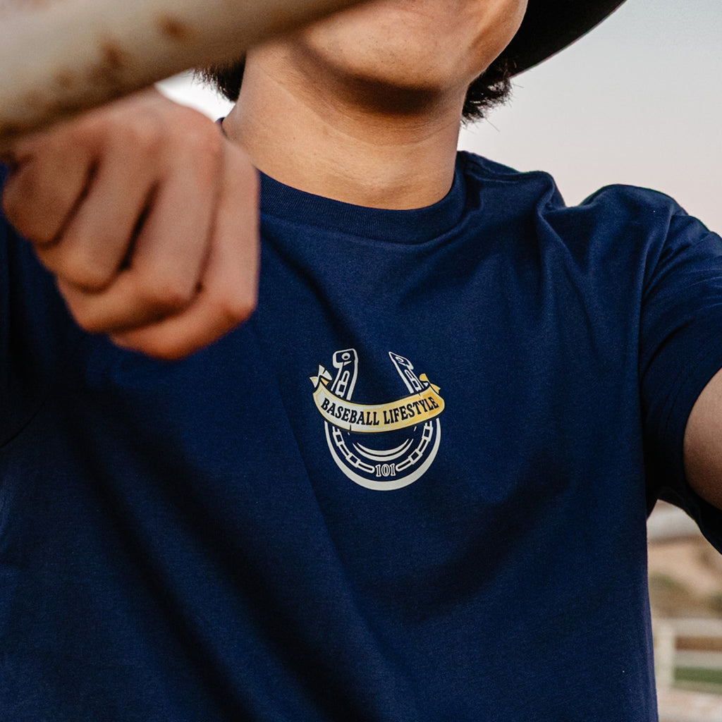 Person wearing a navy blue t-shirt with a Baseball Lifestyle horseshoe logo on the chest.
