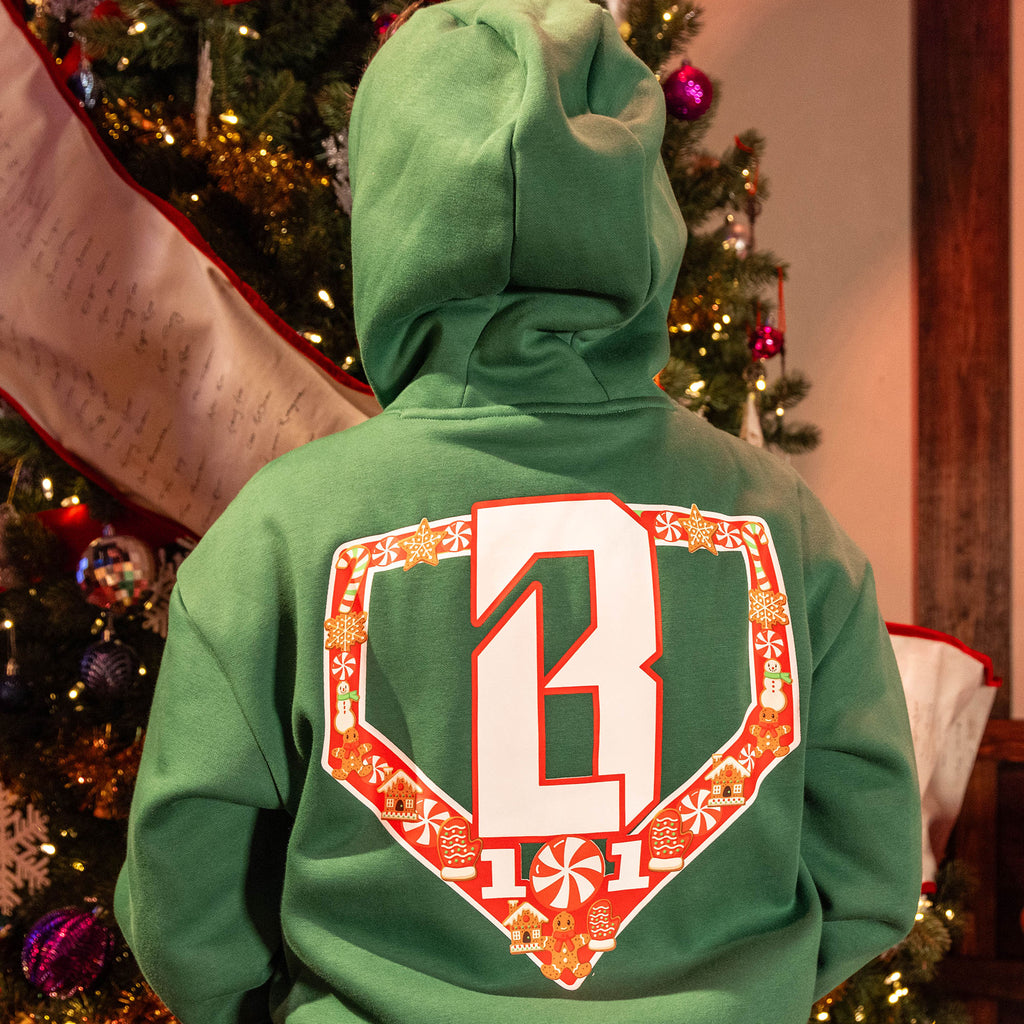 Person wearingGreen hoodie with a festive red and white BL101 logo on back in front of a decorated Christmas tree.