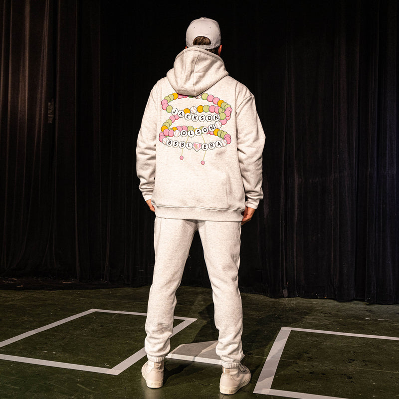 Back view of the adult male model wearing the heather gray BSBL Era sweatpants and hoodie, showing the friendship bracelet graphic with "Jackson Olson BSBL Era" lettering