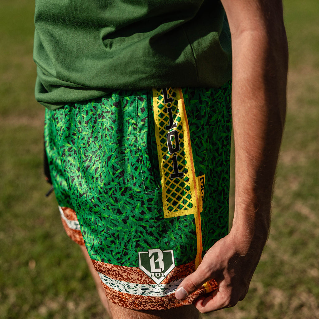 Close up of green grass print mesh shorts with yellow foul pole side stripe BL101 logo patch and brown marbled hem