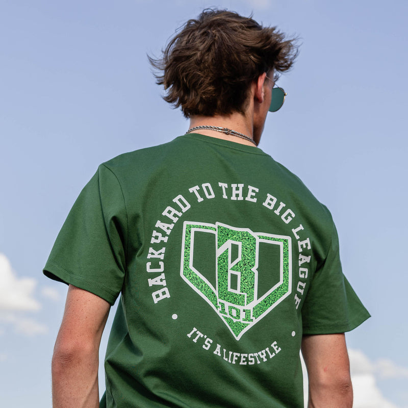 Back view of forest green tee with Backyard to the Big Leagues graphic featuring a grass textured home plate BL101 logo and It's A Lifestyle text