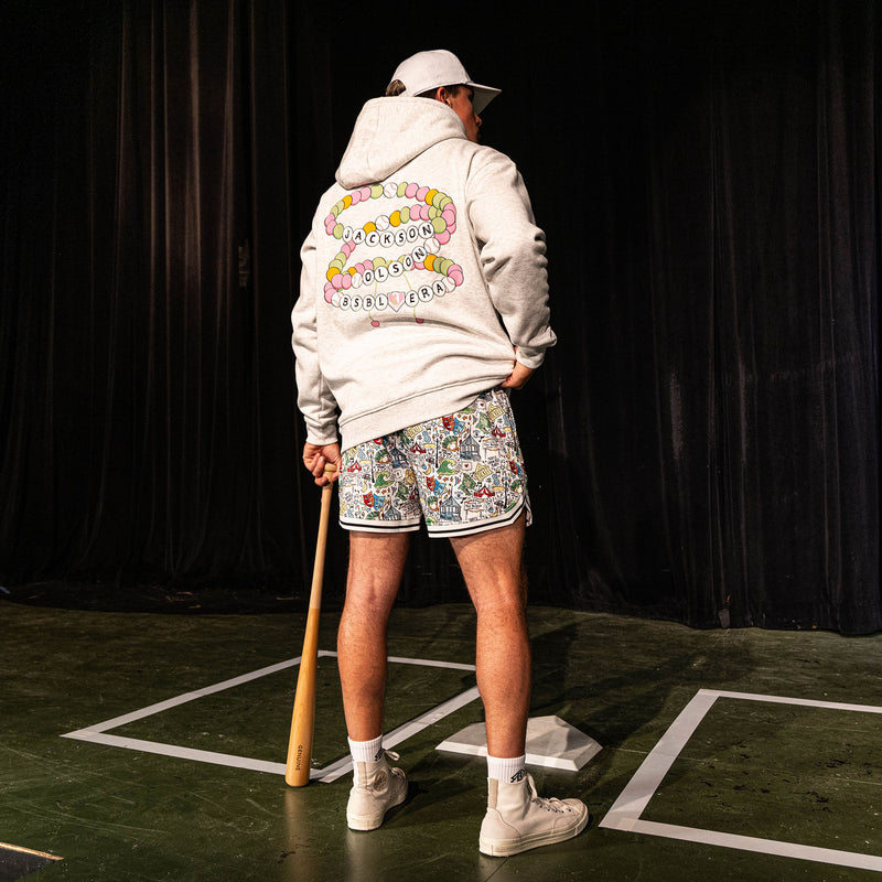 Back view of the adult male model wearing the white Jackson Olson x BL101 Hometown Shorts paired with the BSBL Era hoodie showing the friendship bracelet back graphic