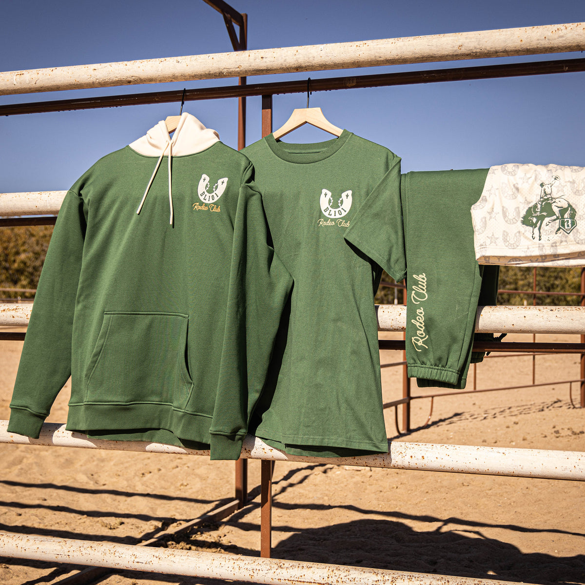 Green sweatshirt and t-shirt with Bl101 horseshoe logos on hangers against railings