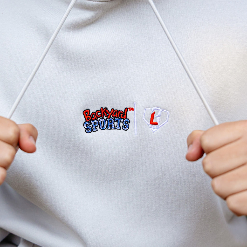White hoodie with 'Backyard Sports' and 'BL1`01' logo, held by two hands.