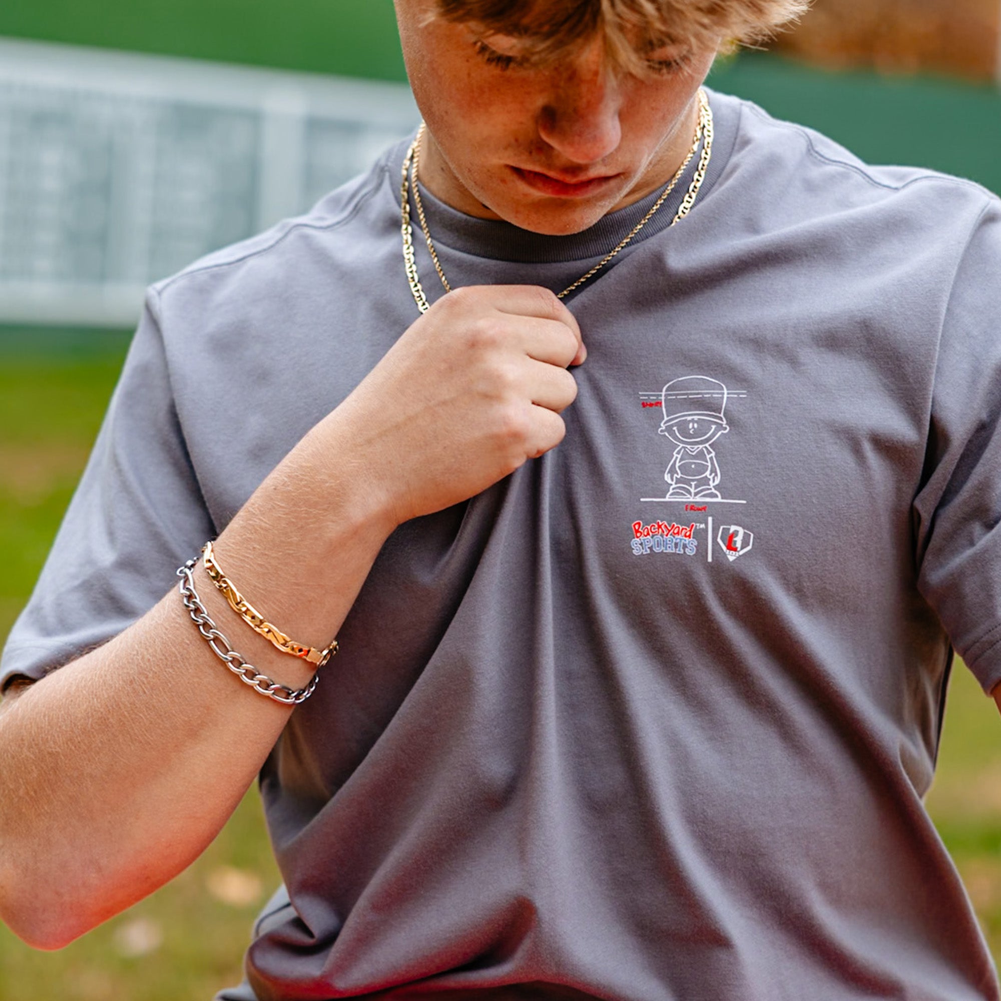 close up of person wearing a gray t-shirt with a Backyard Sports BL101 logo on a sports field
