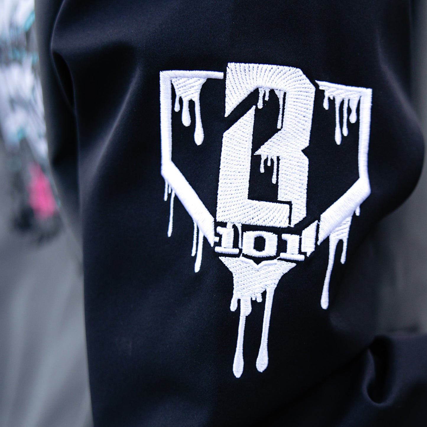 Black and grey hoodie with a white BL101 logo on the sleeve on a blurred background