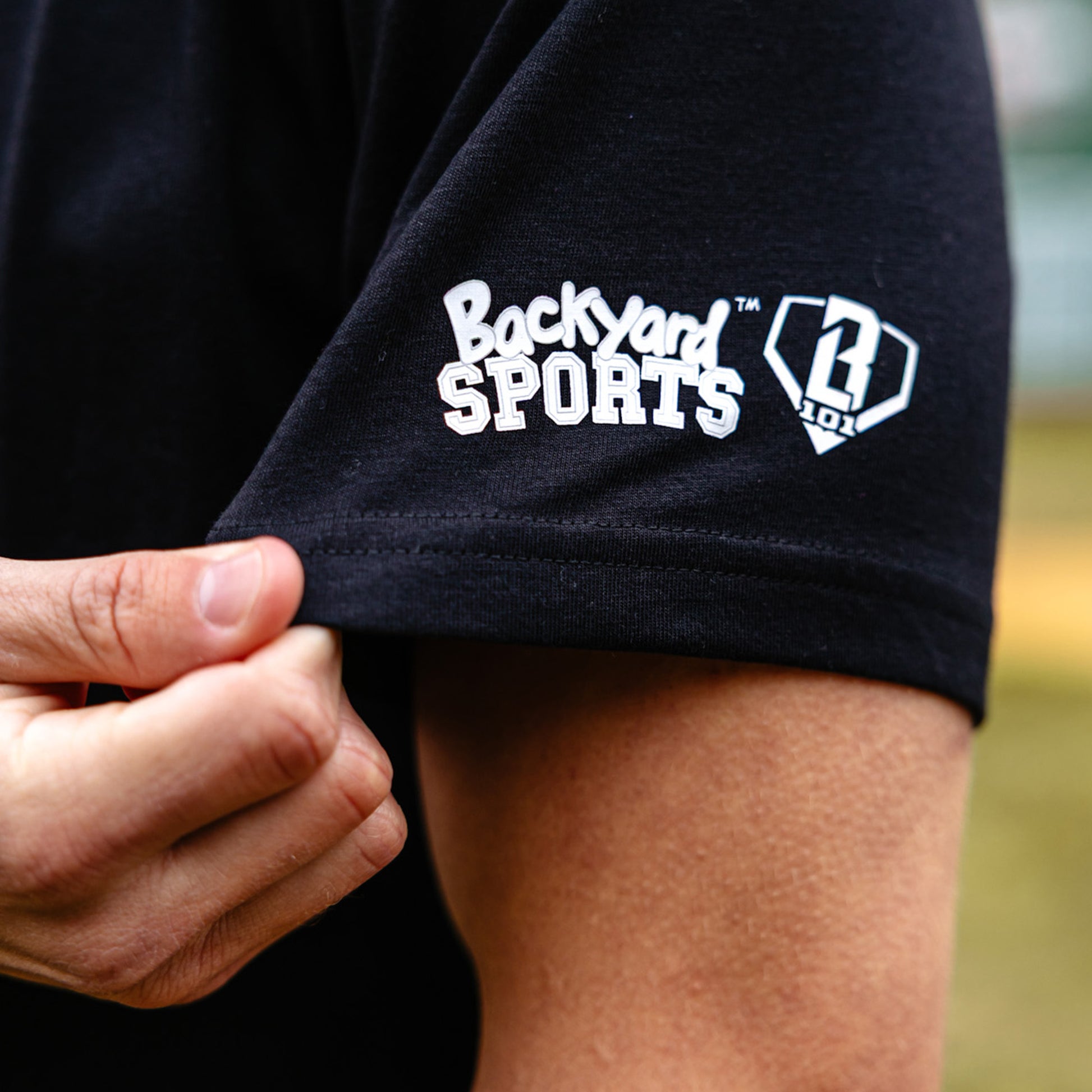 Person wearing a black shirt with 'Backyard Sports' logo, blurred background