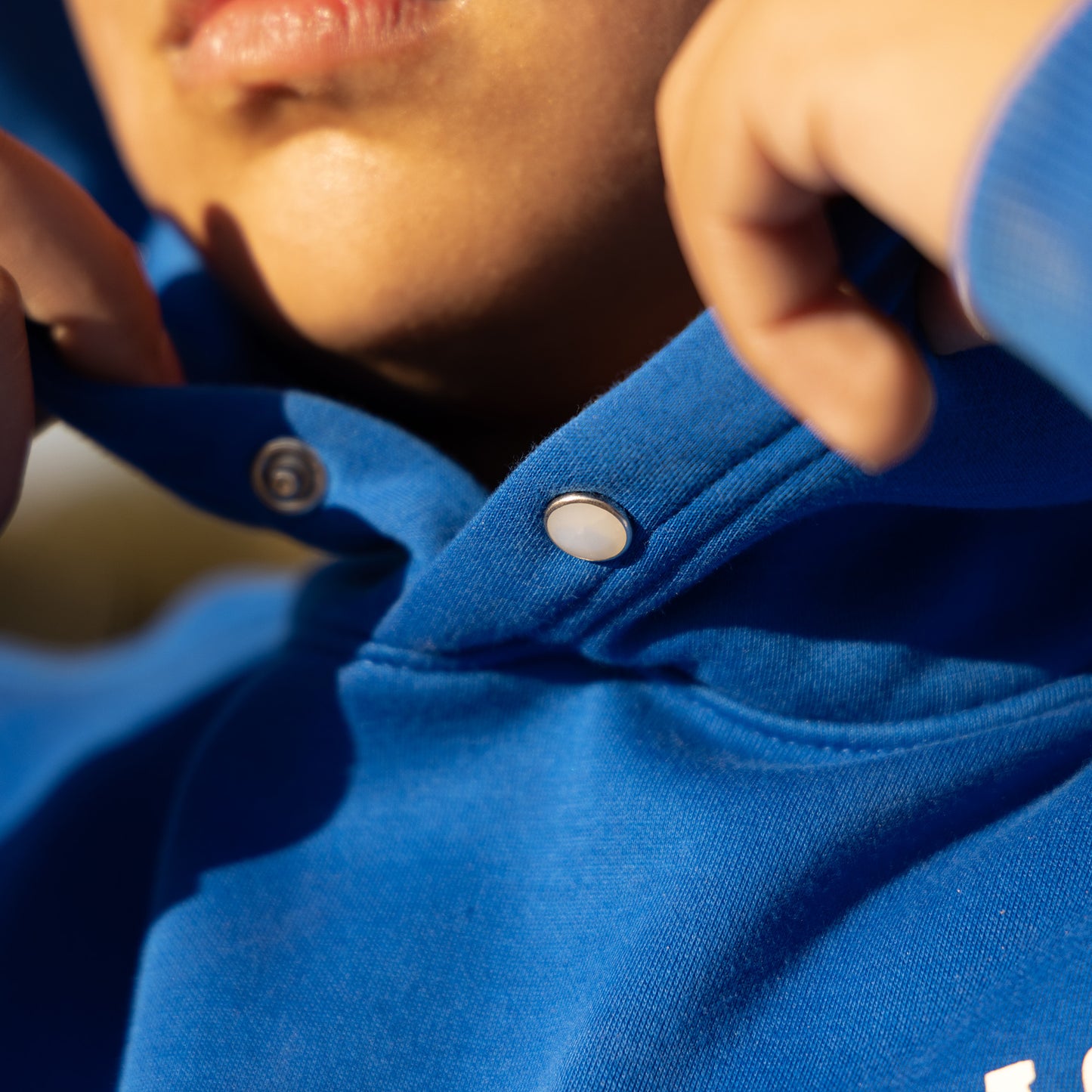 Close-up of a person wearing a blue hoodie with a button being adjusted.