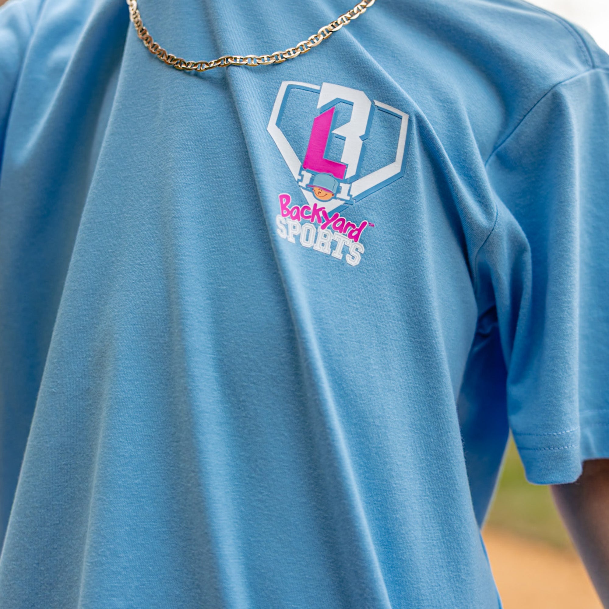 Blue t-shirt with 'BL101 Backyard Sports' logo on a blurred background