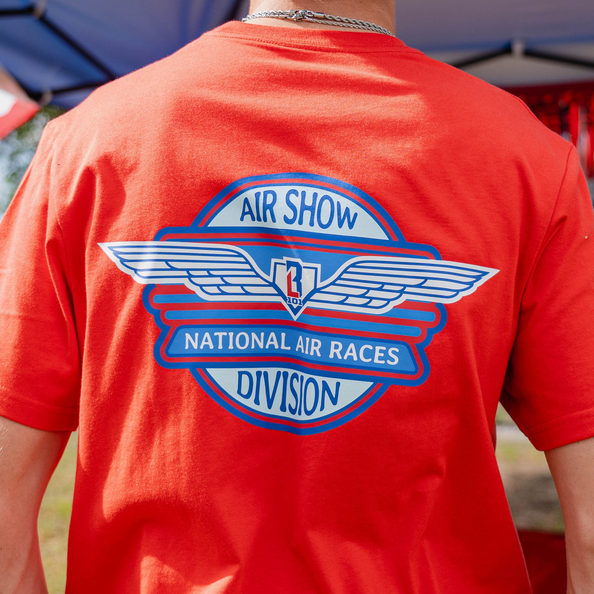 Detail back view of adult male model showing close-up of Air Show National Air Races Division badge on red tee