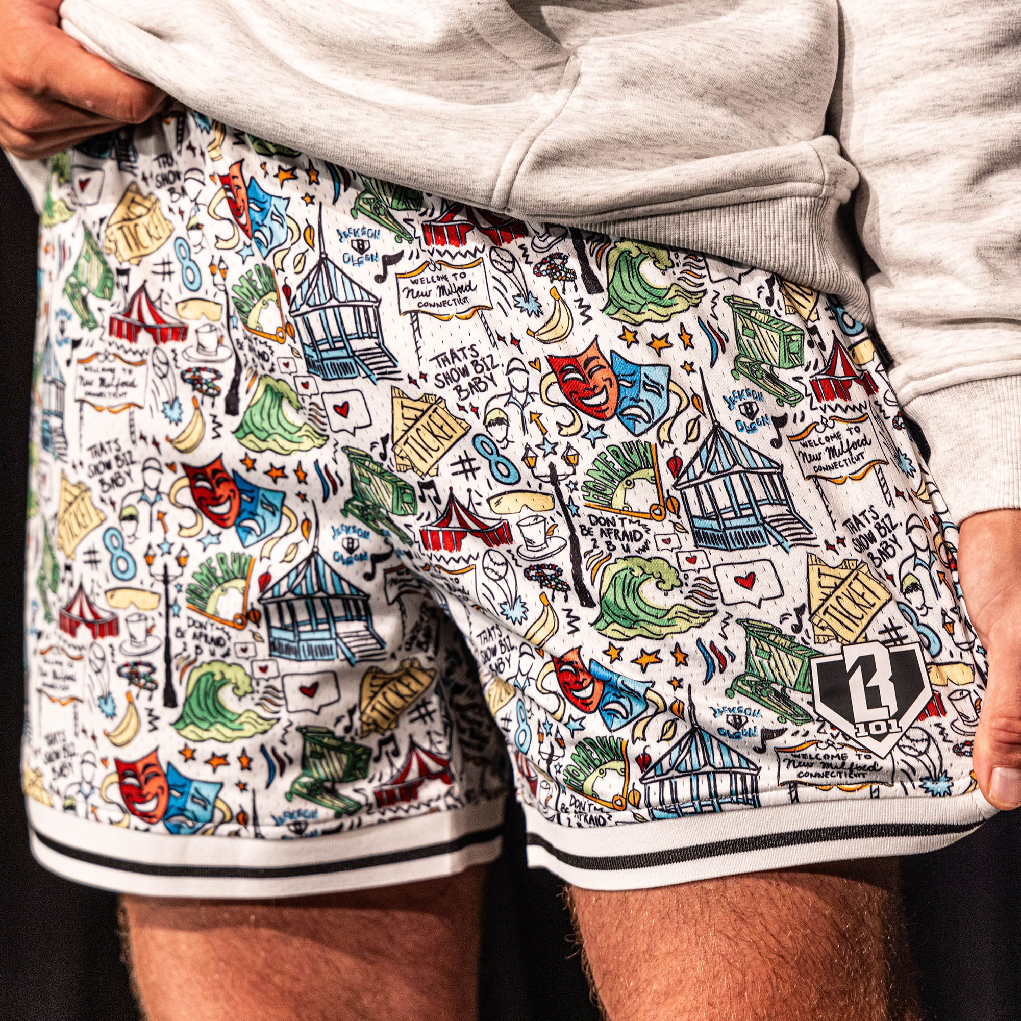Close-up of the white Jackson Olson x BL101 Hometown Shorts highlighting the full all-over illustrated print, striped hem, and BL101 home plate logo