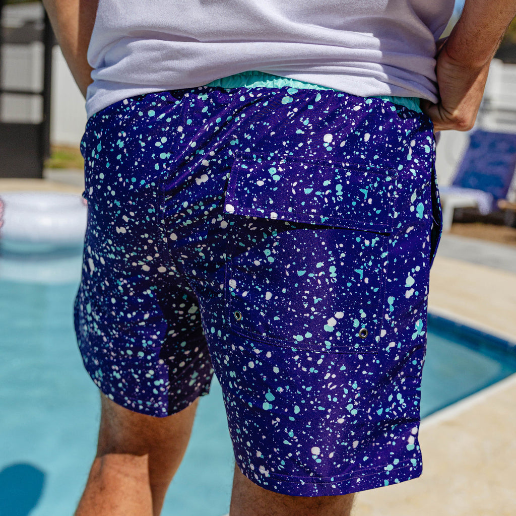Side view of BL101 purple splatter swim trunks worn poolside showing the cargo pocket.